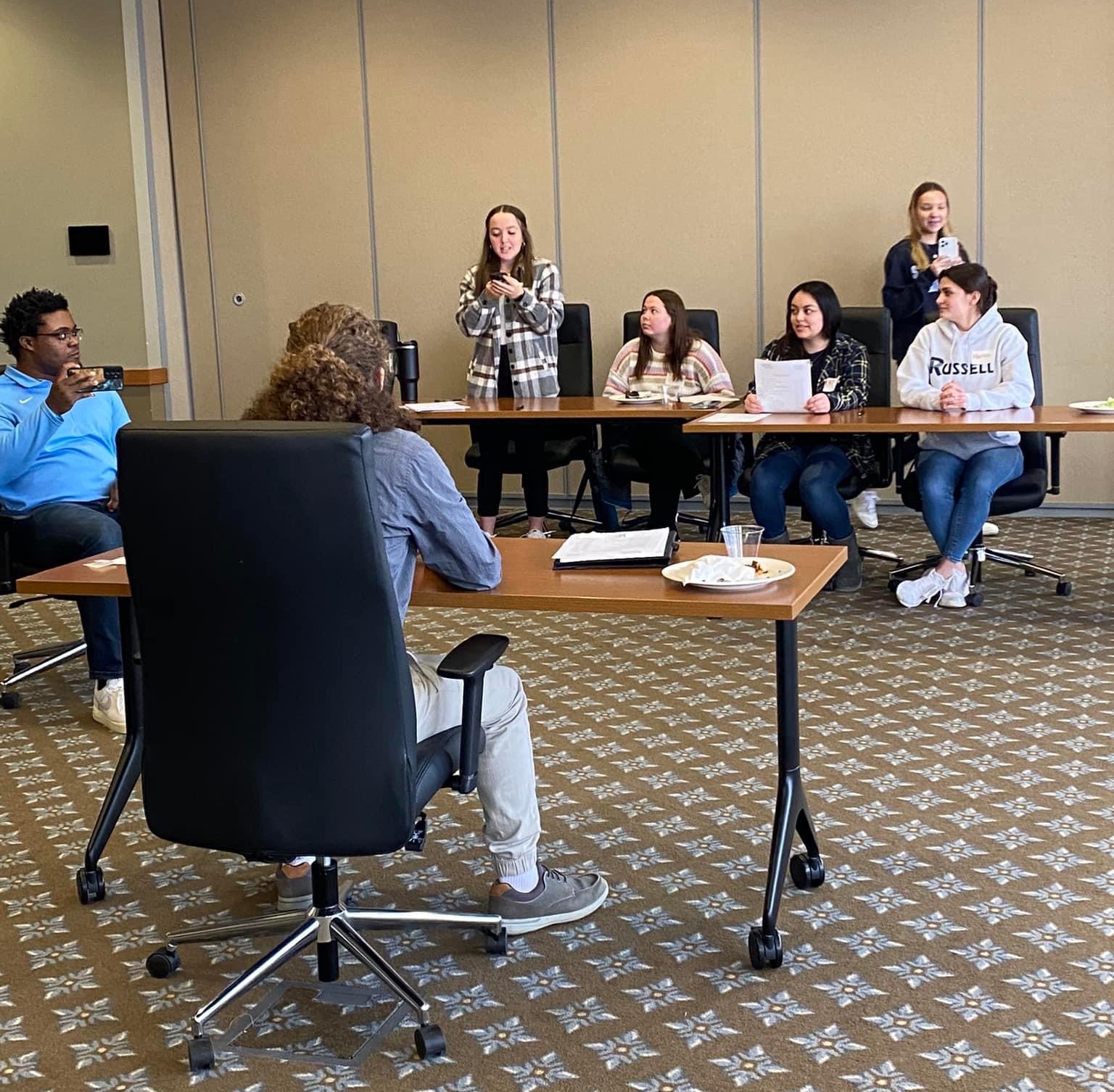 Person standing up to speak next to three others sitting down.