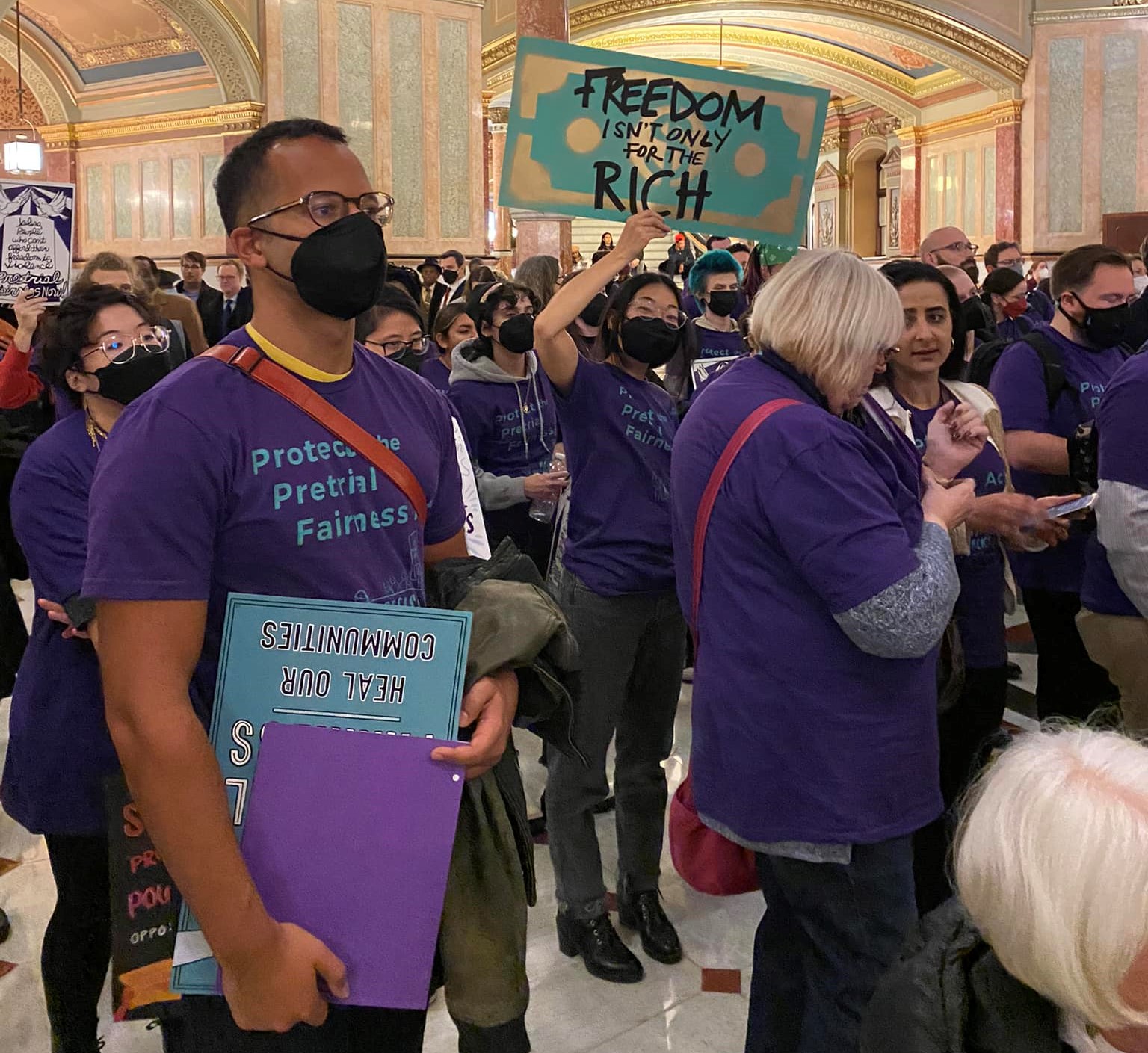 A large group of people protesting inside of a building, with one sign being held up saying 'Freedom isn't only for the rich'.