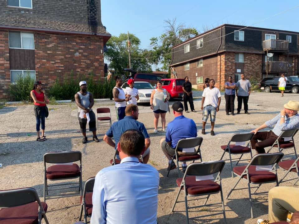 A group of people standing in front of a crowd of four people, who are sitting.